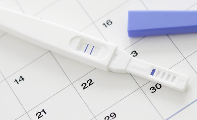 Close up of pregnancy test stick placed on top of a calendar