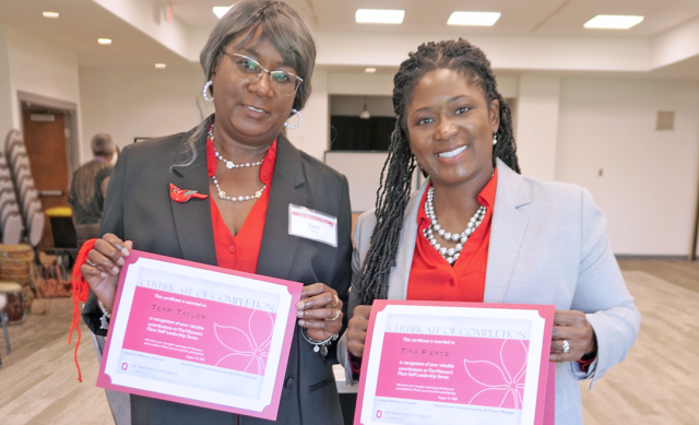 Two women dressed in business clothes standing next to each other smile and hold up certificates of completion.