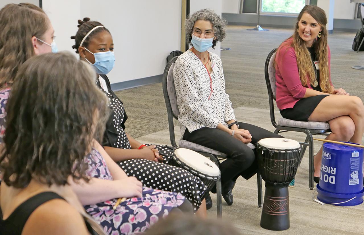 Five women sitting in a larger circle with drums in front of them.